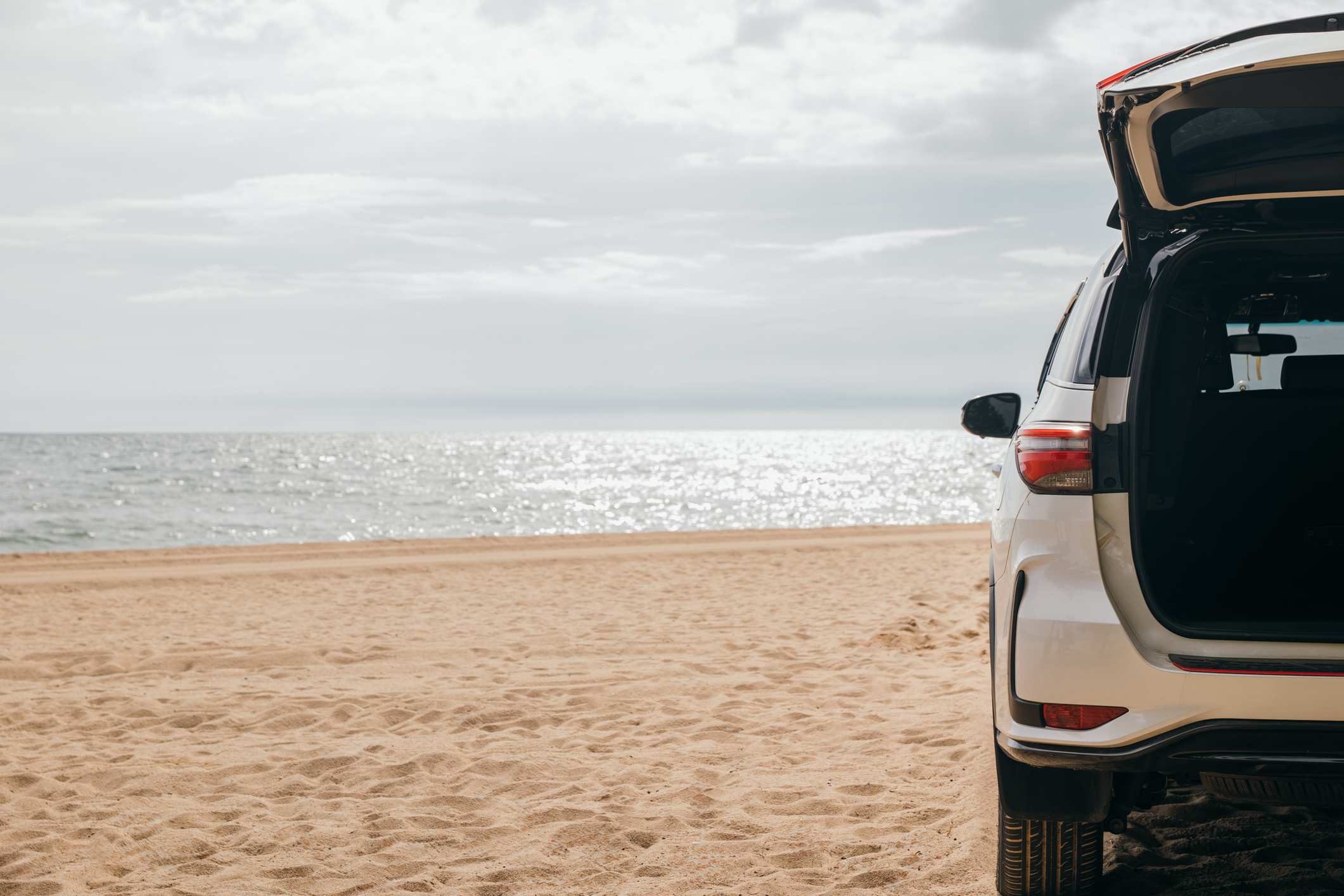 Back end of a white SUV parked on a beach background
